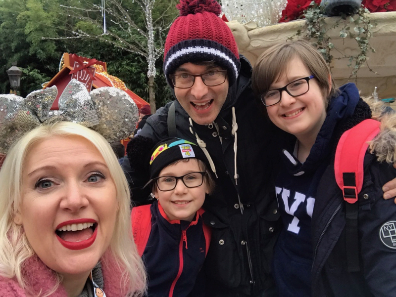 Family selfie - mum, dad, and two boys in winter hats pose in Disneyland Paris