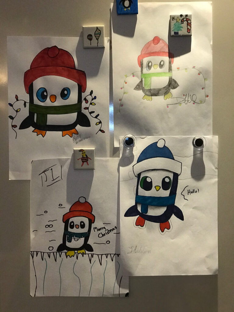 Children's drawings of a penguin, hung on a fridge