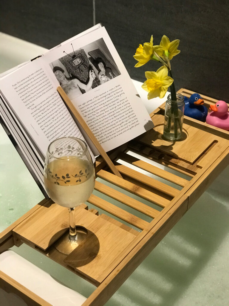 Bath tray over a bath holding wine, book and a flower