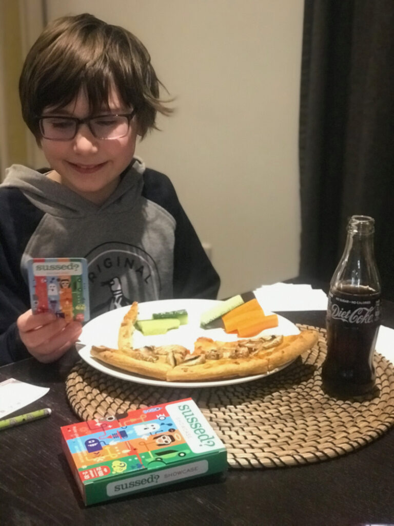 10 year old boy playing Sussed card game and eating a pizza