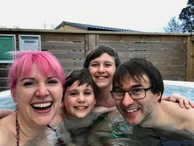 Mom with pink hair, dad and two boys are smiling in a hot tab at their caravan park